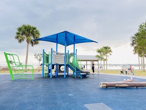 Um parquinho com toldo azul, estruturas de recreação verdes e azuis e um banco.