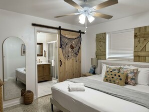 Quarto com cama, ventoinha no teto, porta de madeira e janela com persianas.