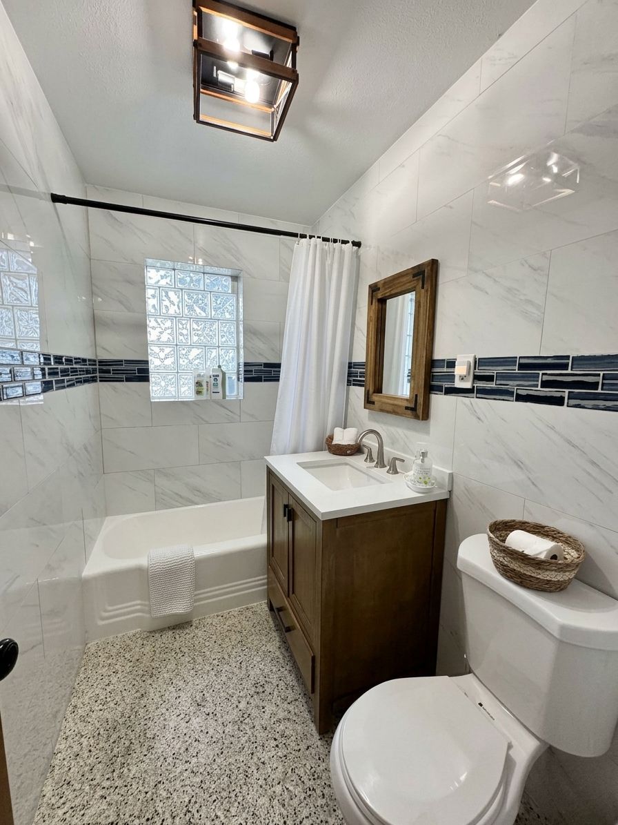 Un bagno con vasca, water, mobile lavabo e una finestra con tenda.