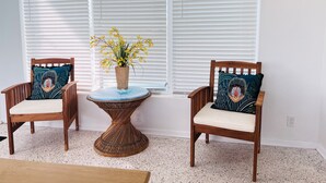 A room with two wooden chairs with cushioned seats and patterned pillows, a small round table with a woven base, and a vase with yellow flowers. - Treasure Coast Pool Home - Walk to Downtown Jensen Beach. (Jensen Beach)