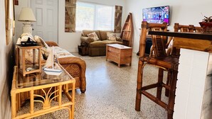 A cozy living room with a sofa, a wooden table, and a television. - Treasure Coast Pool Home - Walk to Downtown Jensen Beach. (Jensen Beach)
