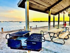 En picknickplats vid stranden med metallgrillar och picknickbord under ett trätak.