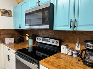 Une cuisine avec des armoires de couleur turquoise, un four à micro-ondes, une cuisinière et divers appareils électroménagers posés sur le plan de travail.