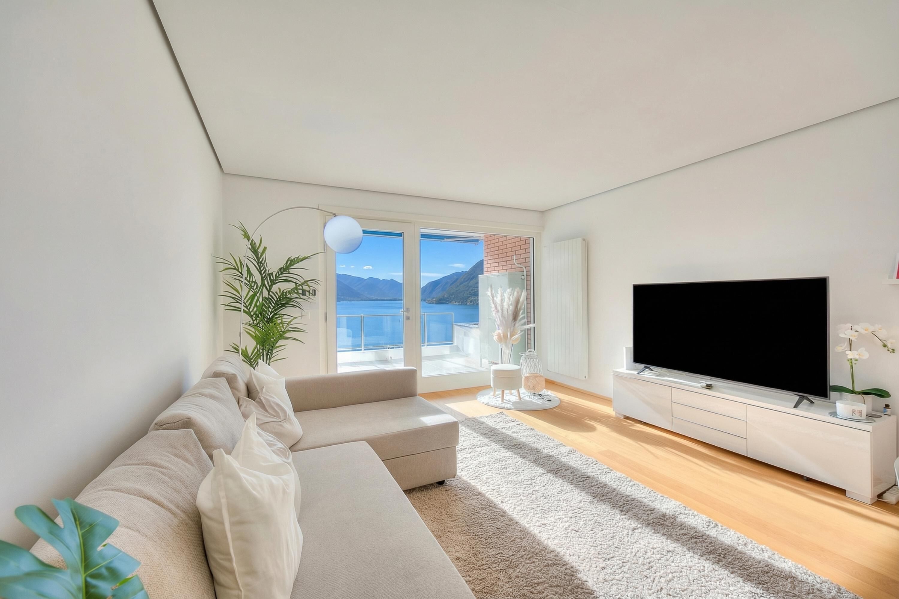 Un salon moderne avec un canapé, un téléviseur à écran plat, une plante et une vue sur l’extérieur.