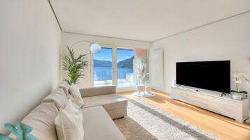 Un salon moderne avec un canapé, un téléviseur à écran plat, une plante et une vue sur l’extérieur.
