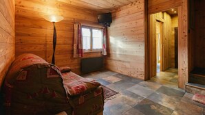 A cozy cabin room with a wooden interior, a bed, a television, and a window with curtains.