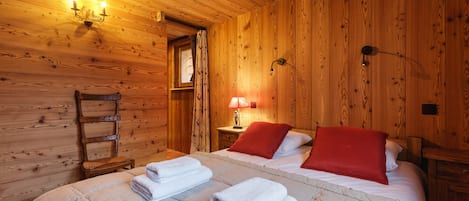 Una habitación de madera con una cama, una mesita de noche, una lámpara y una silla.