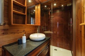 Ein Badezimmer mit einem Holzbadezimmer, einem runden Waschbecken, einem Spiegel und einer Duschkabine.