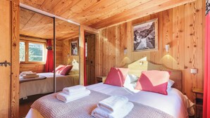 A wooden cabin room with a bed, a mirror, and a window.