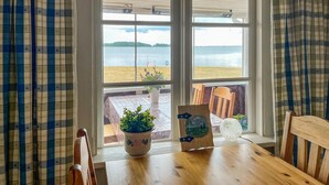 A wooden table with a potted plant and a framed picture in a window seat overlooking a beach.