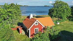 A red house with a sloped roof, surrounded by lush greenery and a large body of water.