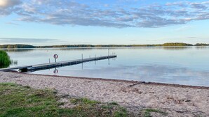 A calm lake with a sandy beach and a wooden pier extending into the water.