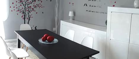 A modern dining area with a black table, white chairs, and a decorative wall with a tree and hearts.