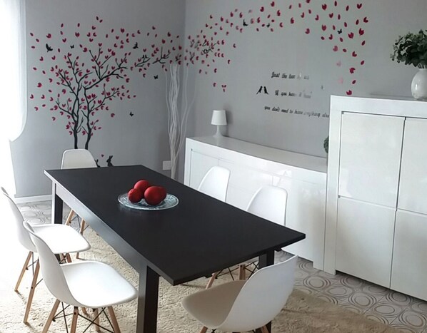 A modern dining area with a black table, white chairs, and a decorative wall with a tree and hearts. - "agli Ulivi" cozy and comfortable apartment (Desenzano del Garda)