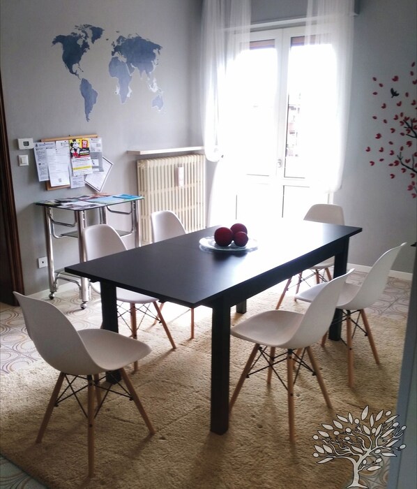 A dining area with a table, chairs, a world map on the wall, a bulletin board, and a radiator.