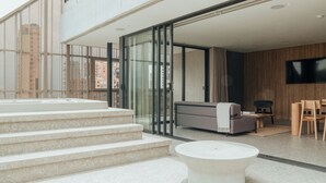 Un intérieur moderne avec une porte vitrée donnant sur un balcon, un canapé, un téléviseur et une petite table.