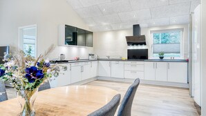 Una cocina moderna con armarios blancos, una campana extractora negra y un comedor con mesa y sillas.