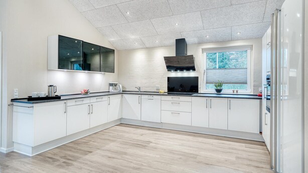 Una cocina moderna con armarios blancos, una campana extractora negra y una ventana con persianas.