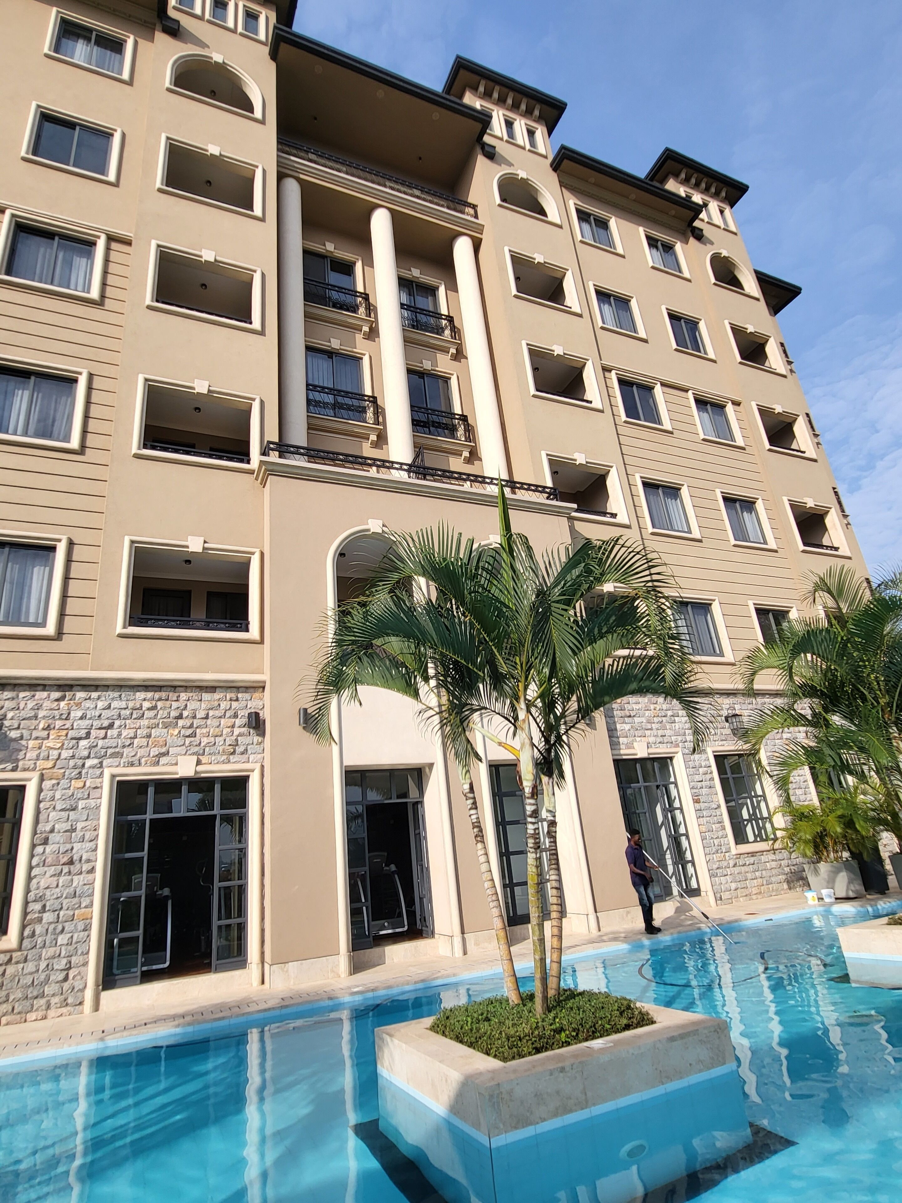 A multi-story hotel with a swimming pool, palm trees, and a stone facade.