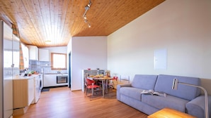 Una cocina moderna con piso de madera, un área de comedor con sillas rojas, un sofá gris y una mesa de madera.
