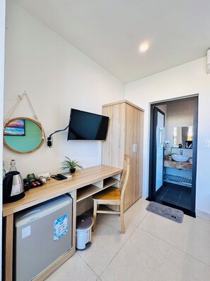 Habitación pequeña con kitchenette, televisor montado en la pared, un armario de madera y una silla.