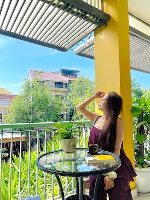 Ein Balkon mit Glastisch, Blumentöpfen und einer gelben Säule.
