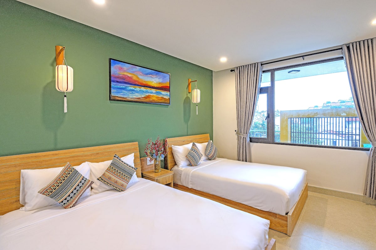 Quarto de hotel com duas camas, um quadro na parede e uma janela com cortinas.