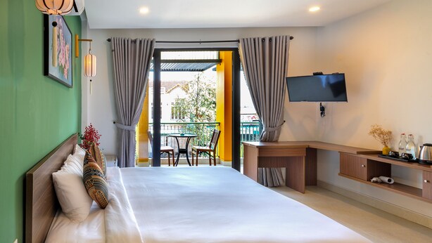 A hotel room with a large bed, a desk, a TV, and a balcony with a view. - HOIANIAN CENTRAL VILLA (Da Nang)
