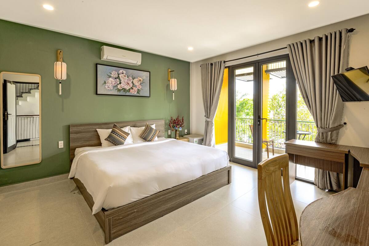 Quarto com cama grande, escrivaninha, cadeira, espelho e varanda com cortinas.