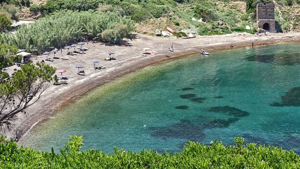 A beach with clear turquoise water, umbrellas, and a few boats.
