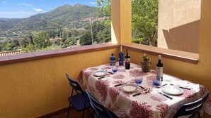 A balcony with a table set for dining, overlooking a mountainous landscape.