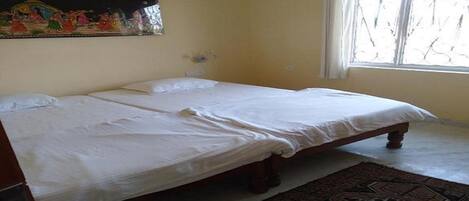 A room with a double bed, a patterned rug, a wall-mounted painting, and a window with curtains.