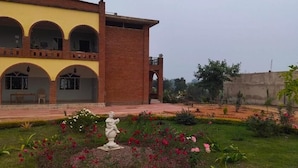 A courtyard with a statue, a building with arches, and a garden with flowers. - Lalita Home Stay (Rajnagar)