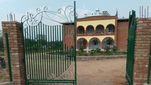 A gated entrance with a brick wall and a building with arched windows in the background. - Lalita Home Stay (Rajnagar)