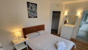 A neatly arranged bedroom with a wooden bed, a nightstand with a lamp, a ceiling fan, a painting on the wall, and a walk-in closet. - Central Motel Mooloolaba Apartments   (Mooloolaba)