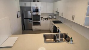 A modern kitchen with white cabinets, stainless steel appliances, and a central island with a sink. - Central Motel Mooloolaba Apartments   (Mooloolaba)