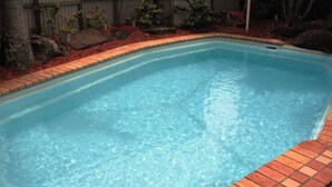 A rectangular swimming pool with clear blue water, surrounded by a brick border and a landscaped area with rocks and small plants. - Central Motel Mooloolaba Apartments   (Mooloolaba)