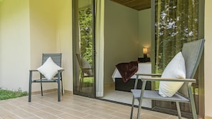 A modern outdoor seating area with two chairs and a table, a sliding glass door leading to a bedroom, and a view of greenery outside. - River Paradise Villa (La Fortuna)