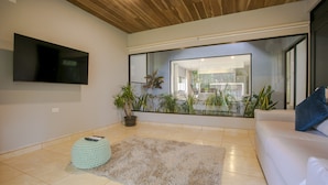 A modern living room with a large mirror reflecting a dining area, a television mounted on the wall, and a potted plant. - River Paradise Villa (La Fortuna)