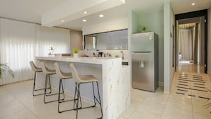 A modern kitchen with a marble countertop, a stainless steel refrigerator, and bar stools. - River Paradise Villa (La Fortuna)