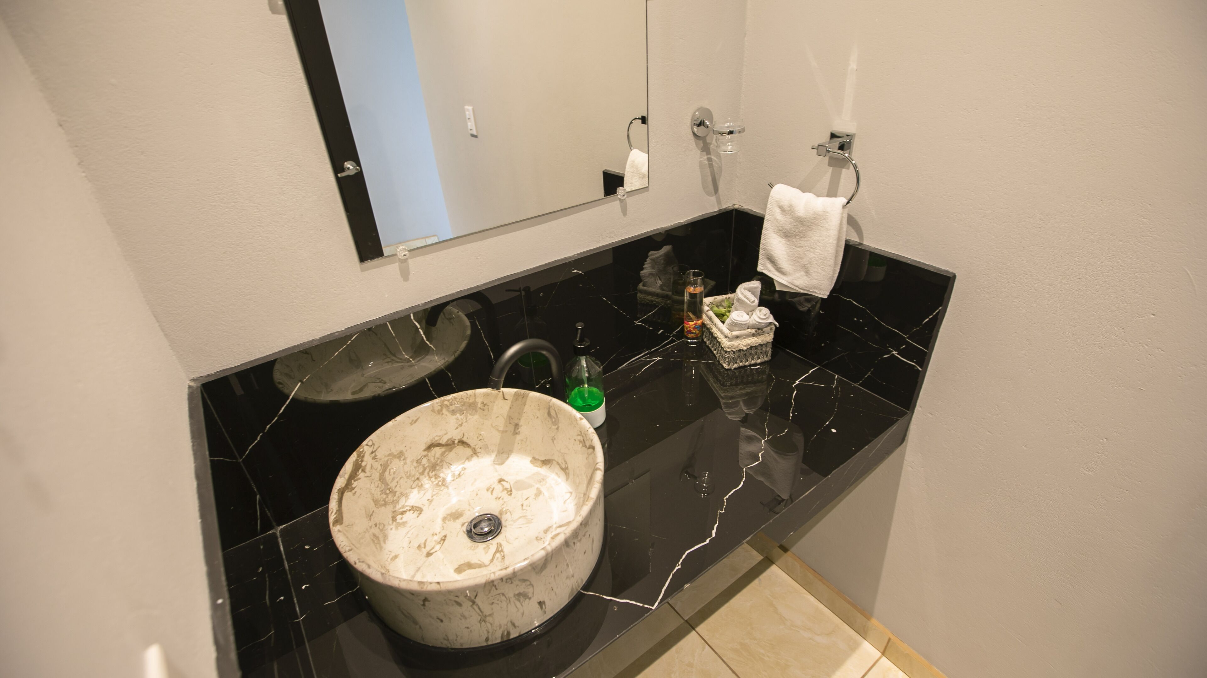Une salle de bain avec un grand lavabo rond, un miroir, un porte-serviettes et un flacon de savon liquide.