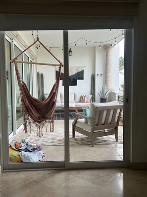 Een kamer met een hangmat, een bank, een stoel en uitzicht door een schuifdeur.