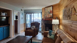 A cozy living room with a fireplace, a television, and a large window.