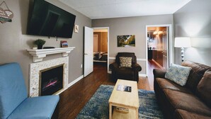 Una sala de estar con chimenea, televisor, sofá, mesa de centro y una silla.