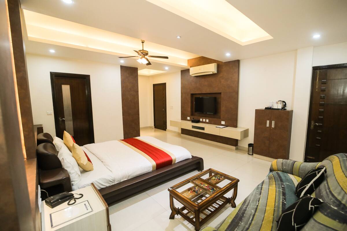 A modern hotel room with a large bed, a sofa, a coffee table, a TV, and a wardrobe.