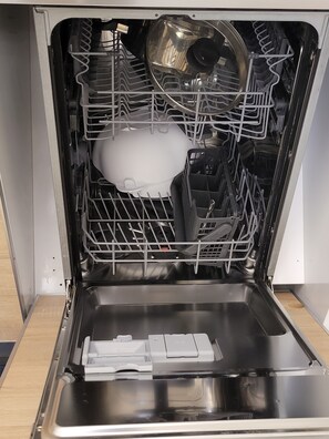 The dishwasher features a stainless steel basin, a transparent water level indicator, and a rack system for holding dishes.