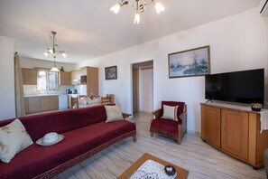 Un salon comprenant un canapé, des fauteuils, un téléviseur et un coin repas avec une table et des chaises.