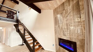 Un interior moderno con una escalera de madera, una chimenea y un techo alto con vigas a la vista.