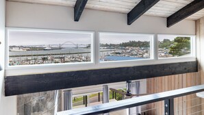 Una habitación con vistas a un puerto deportivo y un puente, vigas de madera en el techo y barandilla de balcón.