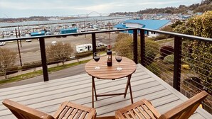 Terraza de madera con dos sillas y una mesa, con vista a un puerto deportivo y un puente.